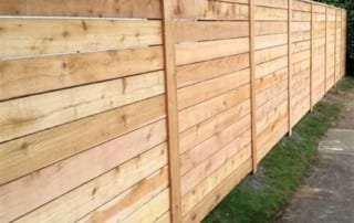 A long wooden fence made of horizontal planks runs alongside a strip of grass and a narrow concrete path.