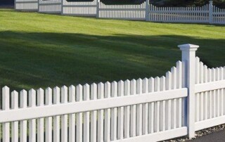 White picket fence bordering a neatly trimmed green lawn, with more sections of similar fencing in the background.